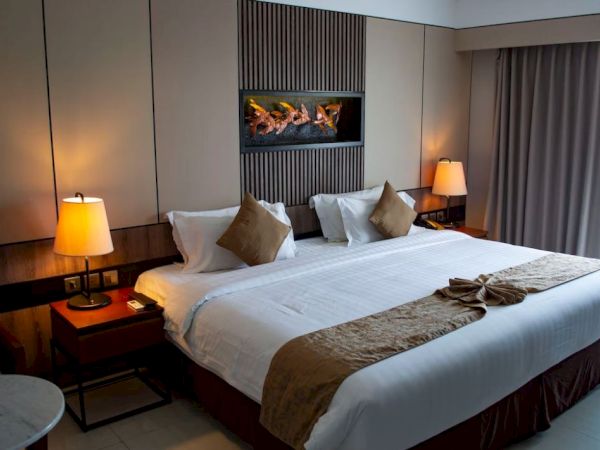 A hotel room with a neatly made king-sized bed, two lamps, a small table, and a window with curtains. The room appears modern and cozy.