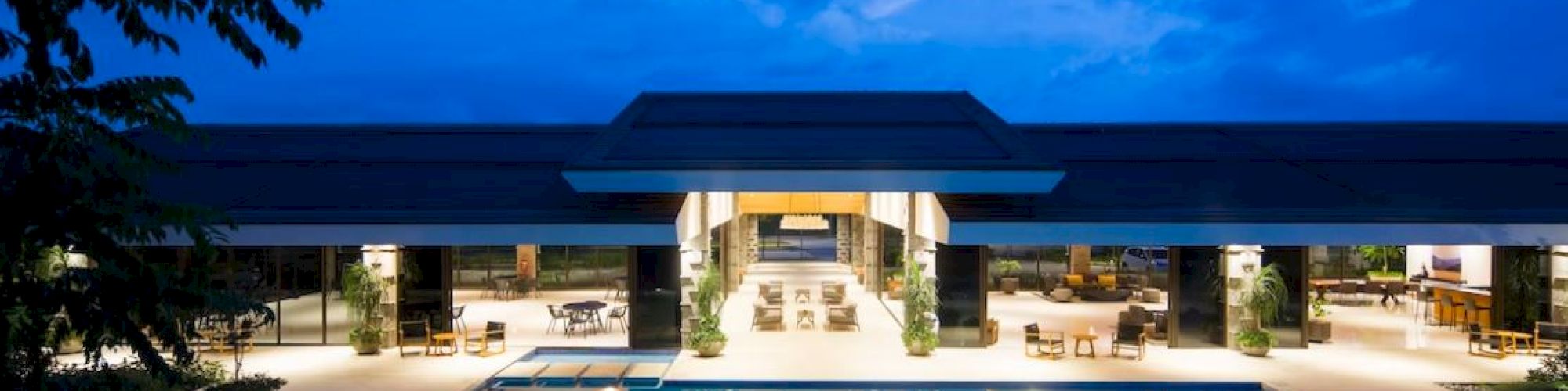 A luxurious outdoor pool area at night, with a modern building and seating areas in the background.