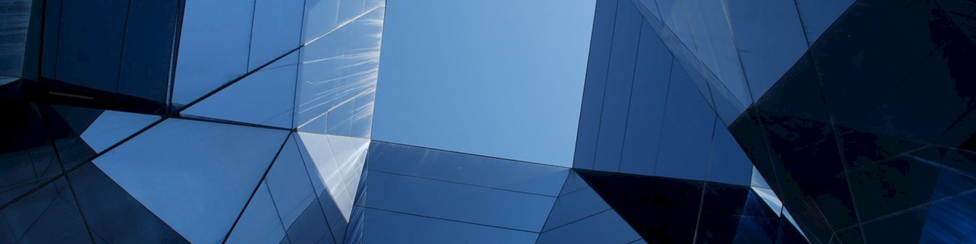 The image shows a geometric arrangement of reflective glass buildings forming a polygonal opening towards the sky.