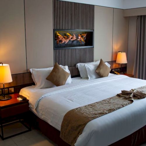 A stylish hotel room with a large bed, decorative pillows, two bedside tables with lamps, and a modern wall feature above the headboard.