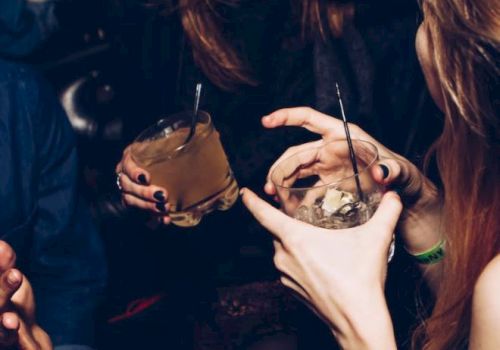 This image shows people socializing, holding drinks. They appear to be having a lively conversation in a dimly lit setting.