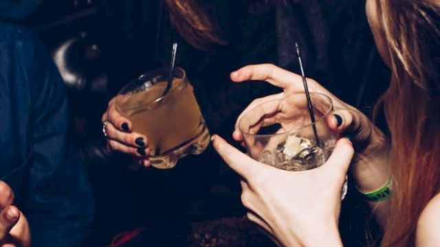 This image shows people socializing, holding drinks. They appear to be having a lively conversation in a dimly lit setting.