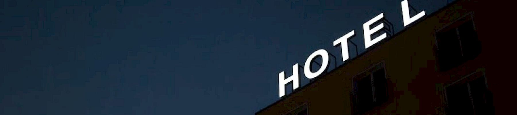 A building with an illuminated "HOTEL" sign at night, with the 'L' slightly tilted, against a dark sky.