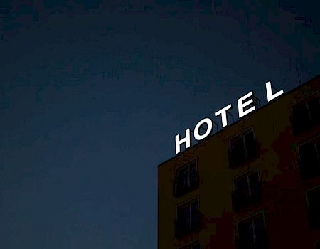 A building with an illuminated "HOTEL" sign at night, with the 'L' slightly tilted, against a dark sky.