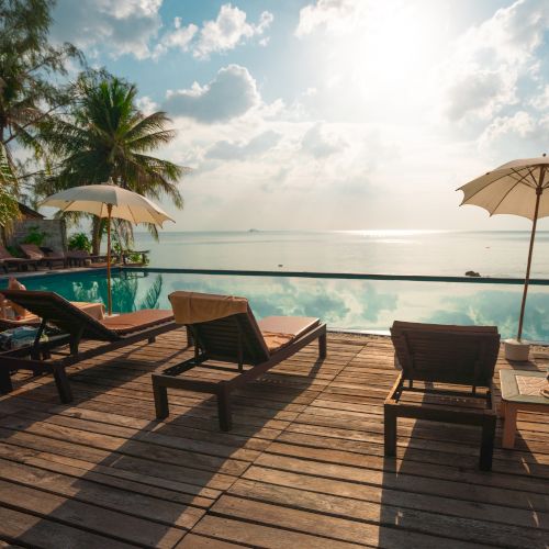 Lounge chairs and umbrellas by an infinity pool overlooking the ocean; palm trees in the background, creating a serene tropical scene.