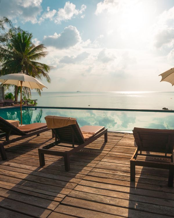 Lounge chairs and umbrellas by an infinity pool overlooking the ocean; palm trees in the background, creating a serene tropical scene.