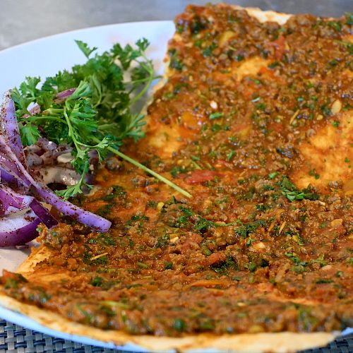 A plate of Turkish lahmacun topped with minced meat and herbs, served with a side of parsley and onion salad.