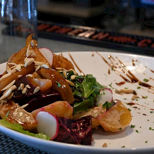 A gourmet salad featuring mixed greens, radishes, almonds, and roasted root vegetables, drizzled with a balsamic glaze on a white plate.