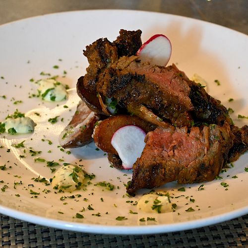 Slices of cooked meat garnished with radish slices and herbs on a white plate, placed on a woven mat.