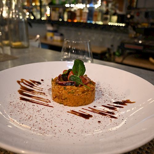 A gourmet dish plated on a white plate, featuring a stacked arrangement garnished with herbs and sauce, presented in a restaurant.