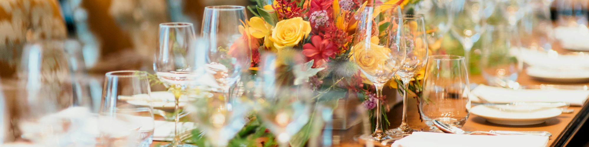 The image shows an elegantly set dining table with neatly arranged plates, glasses, cutlery, and a colorful floral centerpiece.