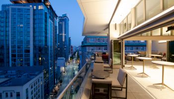 A modern rooftop terrace with seating and tables overlooking a cityscape featuring high-rise buildings during twilight hours.