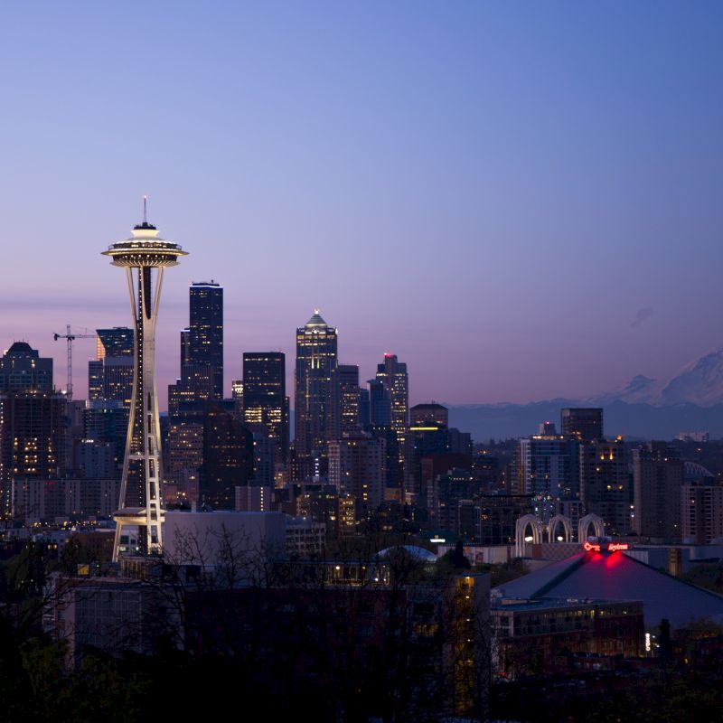 A view of Seattle's downtown skyline at dusk with the Space Needle prominently visible, and Mount Rainier in the background.