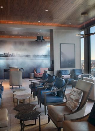 A modern lounge with ample seating, large windows offering a scenic view of a waterfront and ferris wheel, and stylish lighting and decor.