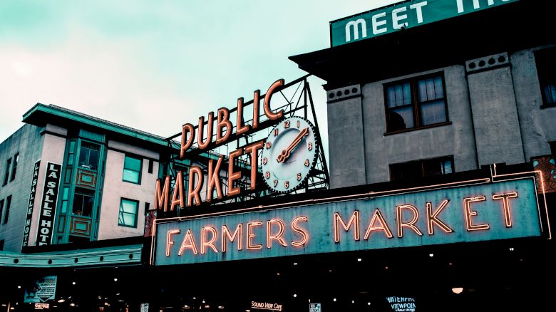 The image shows a public market with neon signs for "Public Market" and "Farmers Market" on the front. An analog clock is also visible.